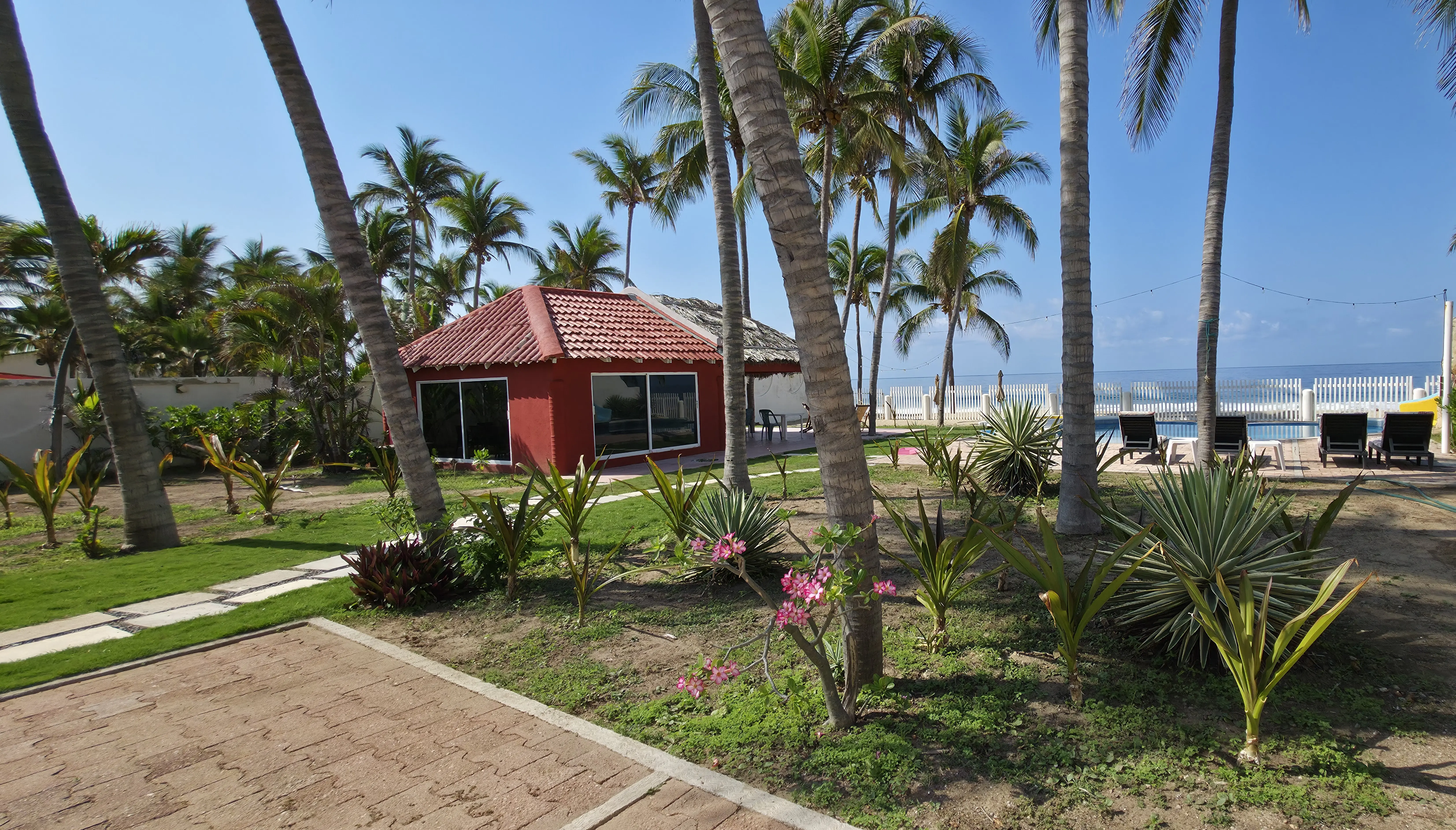 Jardín con palapa roja y vista al océano al atardecer