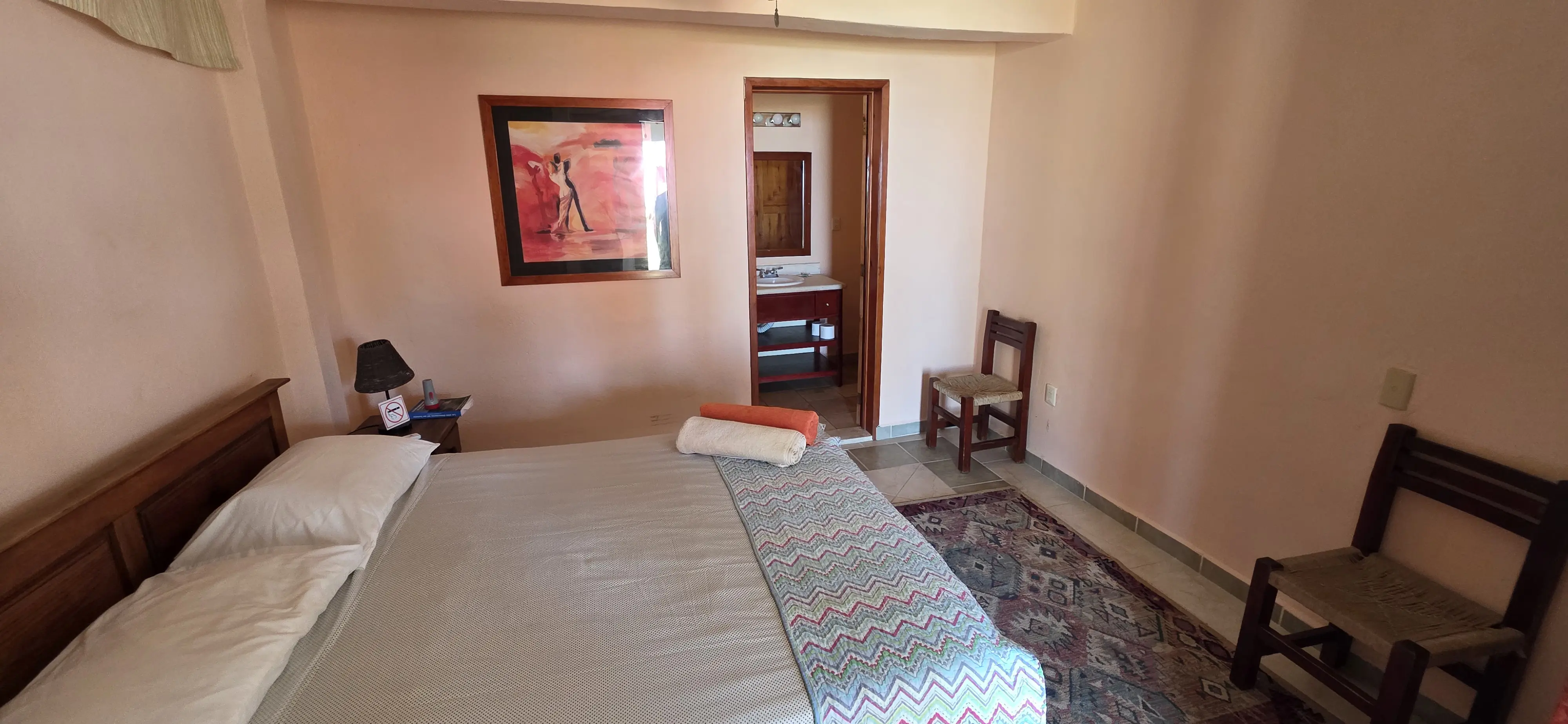 Recámara queen con paredes salmón y vista hacia el baño privado