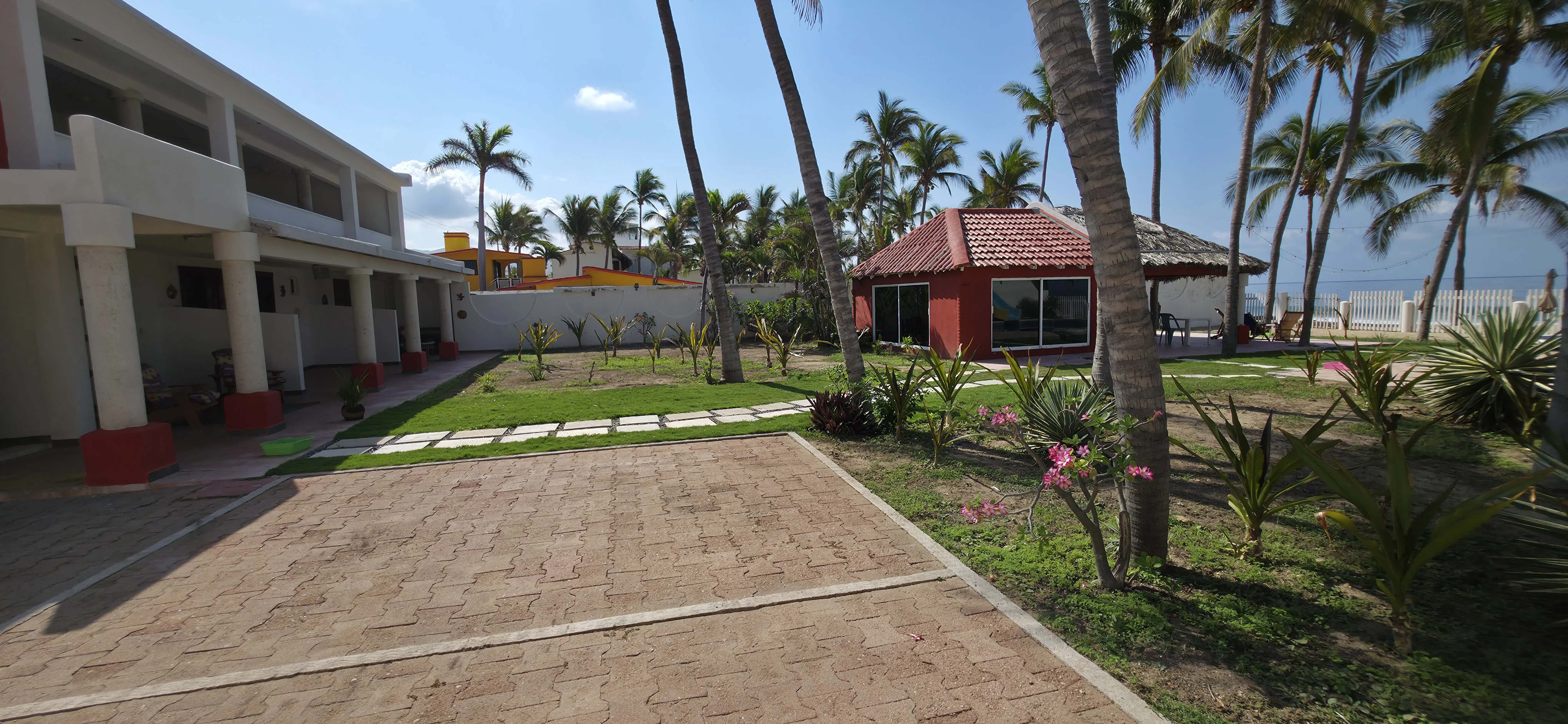 Vista del patio frontal de la villa con acceso peatonal y palmeras